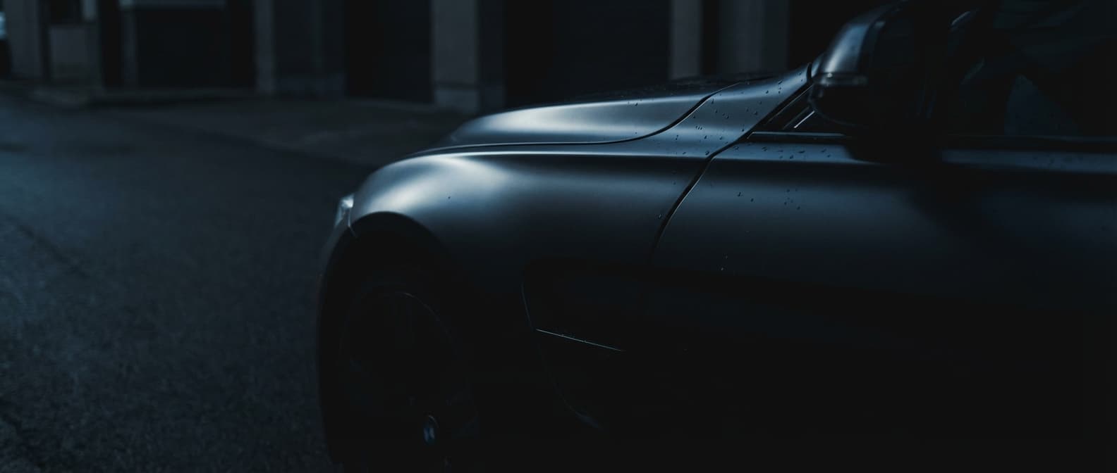 Dark moody close-up of a luxury vehicle with satin vinyl wrap finish